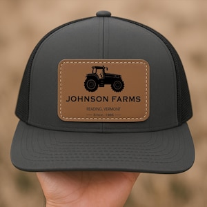 May include: Black trucker hat with a brown leather patch featuring a silhouette of a tractor and the text "JOHNSON FARMS - READING, VERMONT - SINCE 1966".