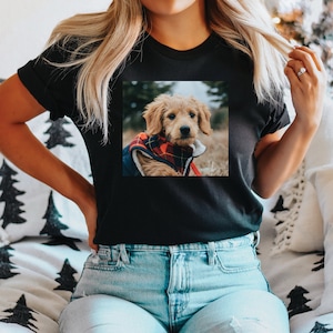 Peut inclure: Un t-shirt noir avec un motif repr&eacute;sentant un chiot brun et blanc portant une veste rouge et noire &agrave; carreaux. Le chiot regarde la cam&eacute;ra.