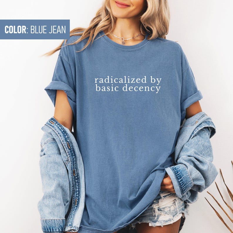 Op de afbeelding: Een jeansblauw T-shirt met de tekst "radicalized by basic decency" in wit gedrukt.