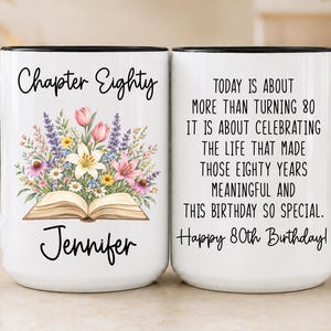 May include: A white ceramic mug with a black handle and rim, featuring a floral illustration emerging from an open book, the text "Chapter Eighty" and "Jennifer" on one side, and a birthday message about turning 80 on the other side.