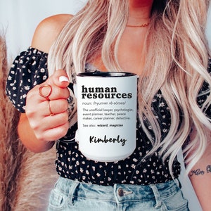 May include: White ceramic mug with a black rim and handle. The mug has black text that reads "human resources" and a definition of the term. The name "Kimberly" is written in black at the bottom of the mug.