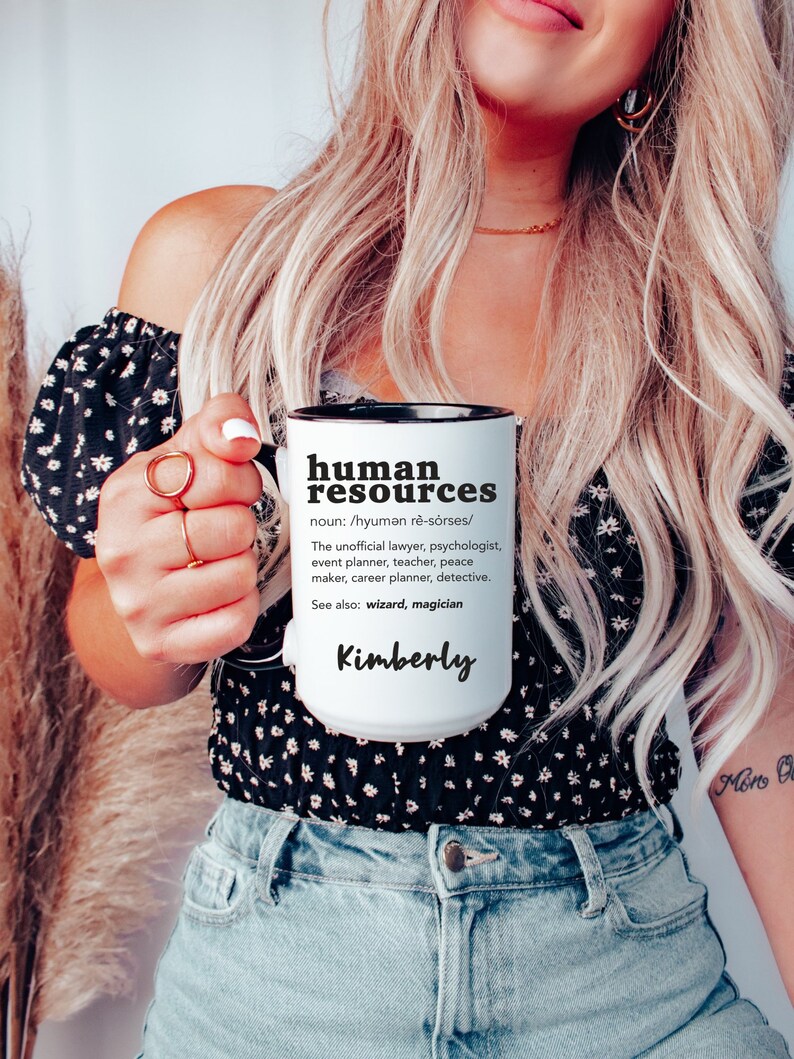 May include: White ceramic mug with a black rim and handle. The mug has black text that reads "human resources" and a definition of the term. The name "Kimberly" is written in black at the bottom of the mug.