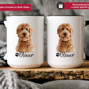 Op de afbeelding: Een witte keramische koffiemok met een zwarte handgreep. De mok heeft een bruine en witte hond met de naam "Oliver" erop gedrukt.