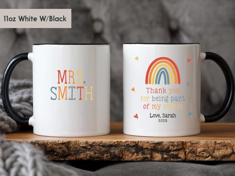 May include: Two white ceramic mugs with black rims. One mug has the text "MRS. SMITH" in colorful letters. The other mug has a rainbow design and the text "Thank you for being part of my story! Love, Sarah 2025".
