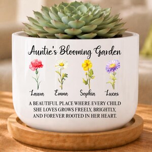 May include: White ceramic planter with a succulent plant. The planter has the text "Auntie's Blooming Garden" and features watercolor illustrations of flowers and names. The bottom of the planter has a quote about love and growth.