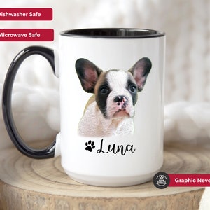 Op de afbeelding: Een witte keramische mok met een zwarte rand en handvat. De mok heeft een kleurrijke illustratie van een Franse bulldog puppy met de naam "Luna" eronder gedrukt. De tekst "Graphic Never Fades" staat gedrukt op de onderkant van de mok.