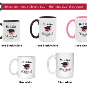 May include: Four white ceramic mugs with black or pink handles. The mugs feature a graduation cap with flowers and the text "Dr. Wilson Phinished 2023". The mugs are available in 11 oz and 15 oz sizes.