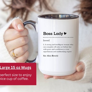 May include: A white ceramic mug with a black interior and handle, featuring the black printed text Boss Lady, a definition of the noun, and the phrase See Also: Beverly. The mug has a capacity of 15 oz as indicated by the text on the image.