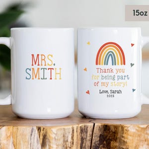 May include: Two white ceramic mugs with handles. One mug has the text "MRS. SMITH" in colorful letters. The other mug has a rainbow design and the text "Thank you for being part of my story! Love. Sarah 2025".