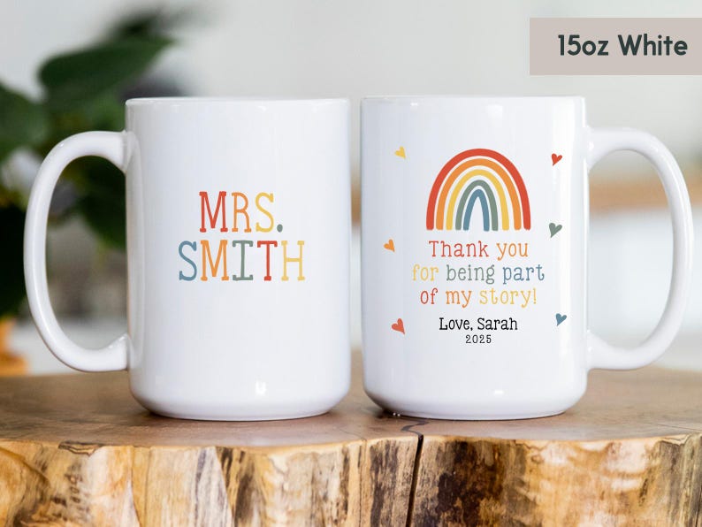 May include: Two white ceramic mugs with handles. One mug has the text "MRS. SMITH" in colorful letters. The other mug has a rainbow design and the text "Thank you for being part of my story! Love. Sarah 2025".