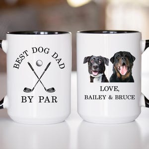 May include: White ceramic mug with black handle and rim. One side features the text "BEST DOG DAD BY PAR" with golf clubs and a ball. The other side has two dog portraits and the text "LOVE, BAILEY & BRUCE".