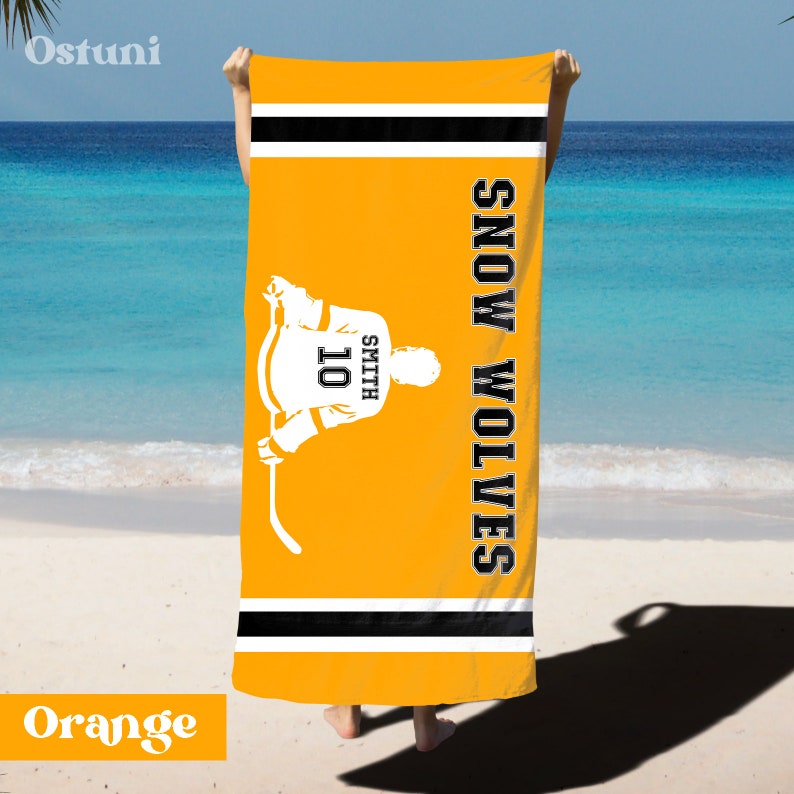 May include: Orange beach towel with black and white stripes. The towel features a hockey player silhouette with the text "Smith 10" on the back and the words "Snow Wolves" vertically down the right side.