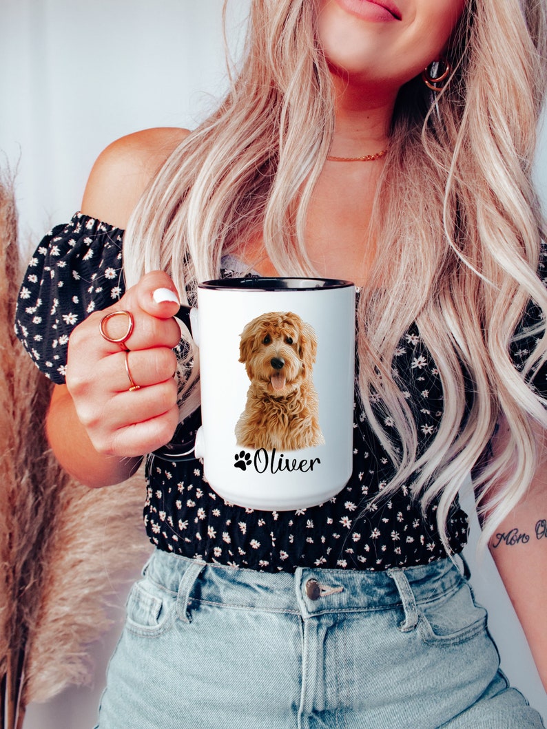 Op de afbeelding: Witte keramische mok met een zwarte rand en handvat. De mok heeft een gekleurde illustratie van een golden doodle hond met de naam "Oliver" gedrukt onder de hond.