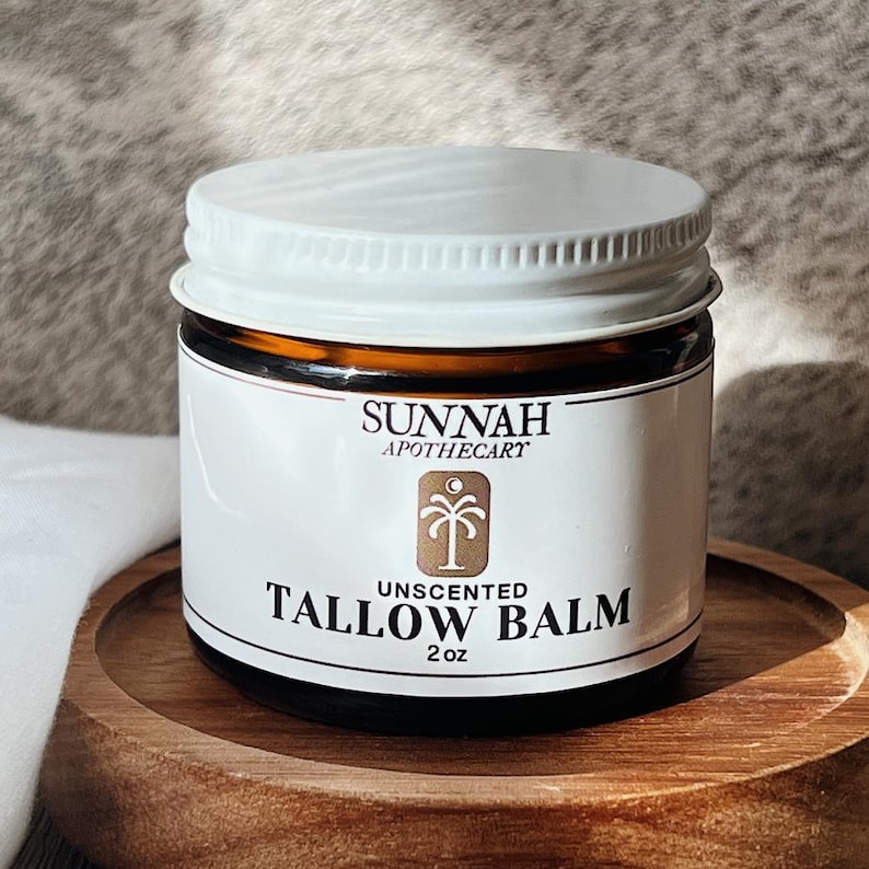 May include: A white jar with a brown label that reads "Sunnah Apothecary" and "Unscented Tallow Balm 2 oz". The label also features a palm tree icon.