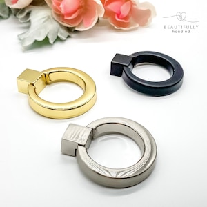 May include: Three ring pulls in gold, silver, and black finishes. The ring pulls are round with a square base.