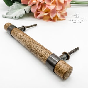 May include: A wooden cabinet pull with a metal band around the centre. The pull has a rustic brown finish and a silver metal band.
