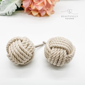 May include: Two beige rope cabinet knobs with a silver metal screw. The knobs are tied in a knot and are a nautical style.