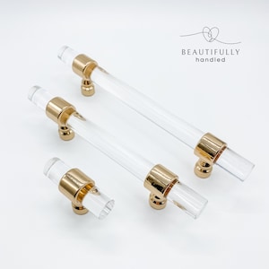 May include: Three clear acrylic cabinet pulls with gold metal accents. The pulls are different sizes. The largest pull is 12.7 cm long. The middle pull is 10.2 cm long. The smallest pull is 7.6 cm long.  BEAUTIFULLY handled.
