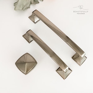 May include: Three silver cabinet hardware pulls, two are long and rectangular with square ends, and one is a small square knob.