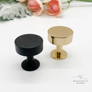 May include: Two cabinet knobs, one black and one gold, with a round top and a cylindrical base.