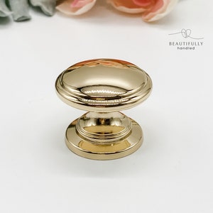 May include: Gold cabinet knob with a round, slightly raised top and a smooth, polished finish.