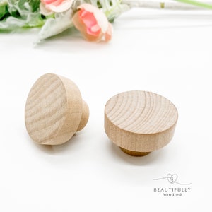 May include: Two wooden knobs with a round, flat top and a cylindrical base. The knobs are made of light brown wood and have a smooth, polished finish.