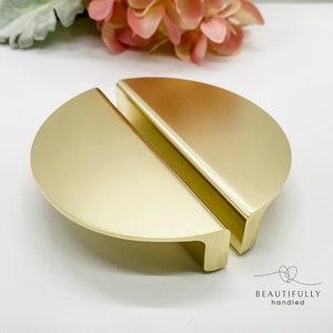 May include: A pair of gold-toned half-circle cabinet pulls. The pulls are made of metal and have a smooth, polished finish.