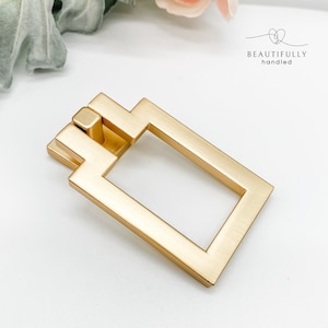 Op de afbeelding: Goudkleurige vierkante kastgreep met een rechthoekige opening. De greep heeft een geborstelde afwerking.
