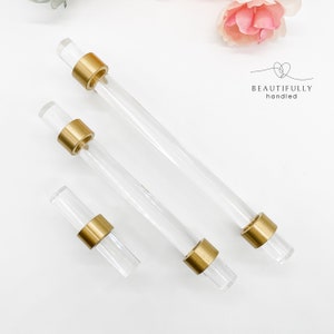 May include: Three clear acrylic cabinet knobs with gold metal accents. The knobs are different sizes.