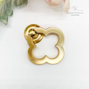 May include: Gold-toned metal cabinet knob with a four-leaf clover design. The knob has a smooth, brushed finish.