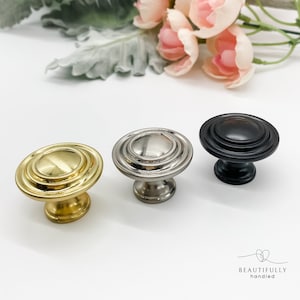 May include: Three cabinet knobs with a circular design. The knobs are in gold, silver, and black.