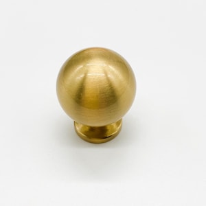 May include: A spherical cabinet knob in a brass finish. The knob has a smooth, polished surface and a round base. This hardware is suitable for drawers, cabinets, and other furniture.