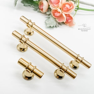 May include: Three gold cabinet pulls with a decorative ring design. The pulls are in various sizes and are shown on a white surface.