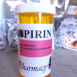 May include: A yellow plastic pill bottle with a white lid and a label that reads "PIRIN" in black letters. The label also includes the text "Take with water. Use only when you feel you can't go on." and "Pharmacy" in a decorative font.