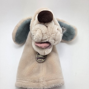 May include: A plush dog hand puppet with a beige body, a brown nose, and blue-grey ears. The puppet has a pink tongue and a tag that reads "WRINKLES" and "827846".