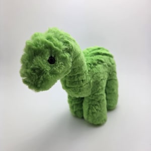 May include: A plush green dinosaur toy with a textured, fuzzy exterior. The toy has a long neck, four stubby legs, and a small black eye. The dinosaur is made of a soft, fuzzy material.