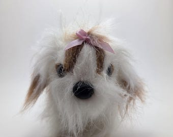 Op de afbeelding: Een pluchen speelgoedhond met witte vacht, bruine vlekken en een roze strik. De hond heeft zwarte ogen en een zwarte neus. Het speelgoed is ontworpen om op een Shih Tzu of een vergelijkbaar ras te lijken.