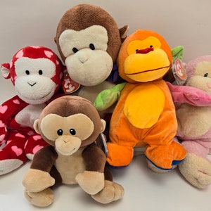 以下が含まれることがあります： さまざまな色とポーズのぬいぐるみのおさるさん5体。おさるさんは茶色、赤、オレンジ、ピンク、茶色です。大きな目と笑顔をしています。おさるさんはみんなTyタグをつけています。