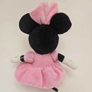 Puede incluir: Juguete de peluche rosa y negro de un rat&oacute;n de dibujos animados con un lazo rosa. El rat&oacute;n lleva un vestido rosa y tiene la cara blanca.