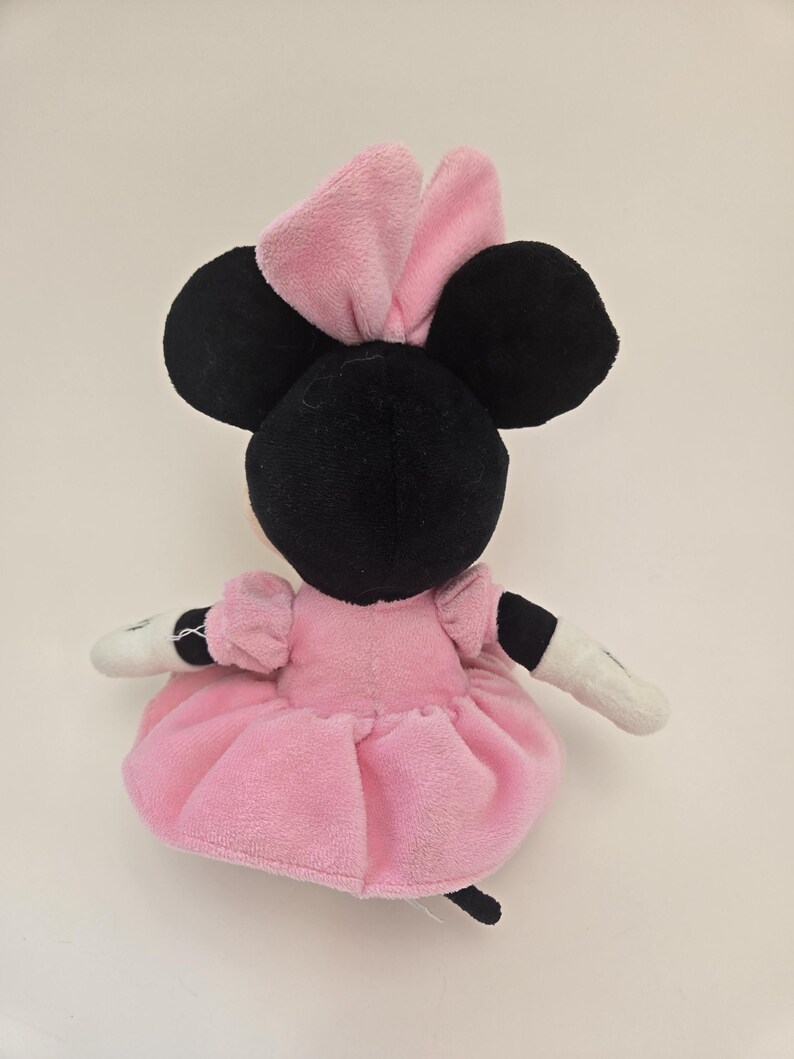Puede incluir: Juguete de peluche rosa y negro de un rat&oacute;n de dibujos animados con un lazo rosa. El rat&oacute;n lleva un vestido rosa y tiene la cara blanca.