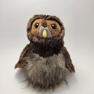 May include: A plush owl toy with large black eyes, a yellow beak, and brown and gray feathers. The owl has a soft, furry texture and is designed to resemble a real owl. The toy is suitable for children and collectors.