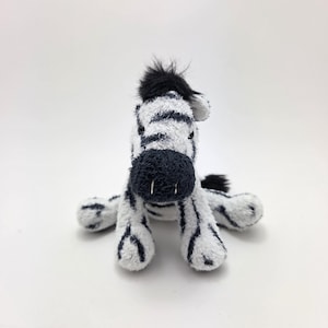 May include: A plush zebra toy with black and white stripes. The zebra has a black mane and a black nose. The toy is sitting on a white background.