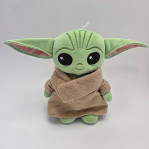 May include: Green plush toy with large ears, brown eyes, and a brown coat. The toy is a character from the Star Wars franchise.