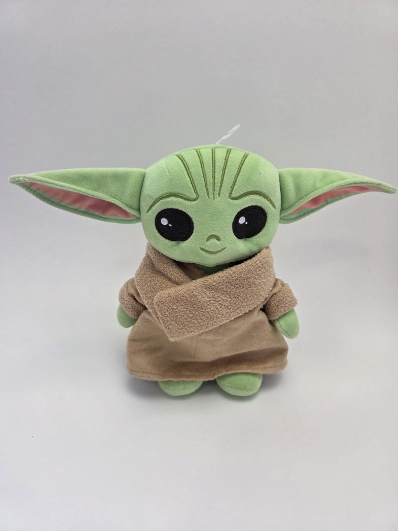 May include: Green plush toy with large ears, brown eyes, and a brown coat. The toy is a character from the Star Wars franchise.