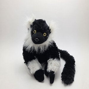 Può includere: Un peluche di lemure nero e bianco con occhi gialli e una lunga coda nera. Il lemure ha la pelliccia bianca intorno al viso e sulle zampe. Il giocattolo è progettato per assomigliare a un lemure dalla coda ad anelli.