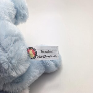 May include: A light blue plush toy with a tag that reads "Disneyland Resort Walt Disney World." The toy has a soft, fluffy texture and is partially visible in the image. The tag also features a circular logo.
