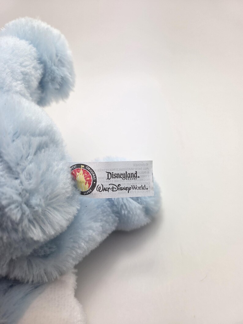 May include: A light blue plush toy with a tag that reads "Disneyland Resort Walt Disney World." The toy has a soft, fluffy texture and is partially visible in the image. The tag also features a circular logo.