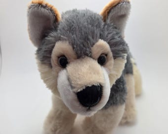 May include: A plush wolf toy with a realistic design. The toy features a gray and tan fur with black eyes and a black nose. The ears have brown tips. The wolf is standing on all fours.