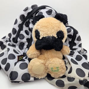 May include: A black and white polka dot backpack with a beige and black plush pug stuffed animal inside. The backpack has a zipper closure and a green tag that says "Pet Sac".