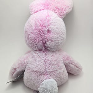 May include: A pink plush bunny rabbit toy with a white fluffy tail. The bunny has a soft, fuzzy texture and is sitting on a white background.